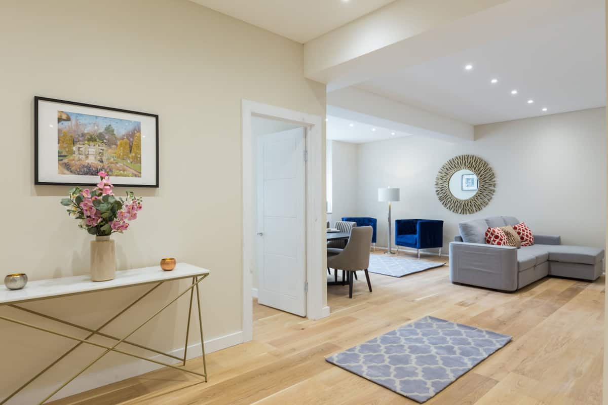 A modern living room with a grey sofa, a coffee table, and a dining area in the background.