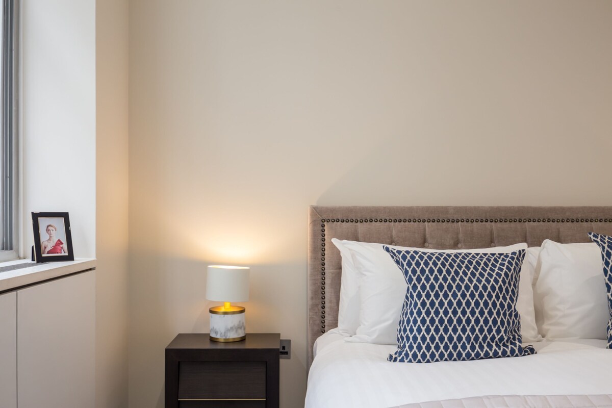 A neatly made bed with patterned pillows, a bedside lamp, and a framed photo on a nightstand.