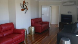 Una sala de estar con dos sofás de cuero rojo, un sofá negro, un televisor y un elemento decorativo en la pared.