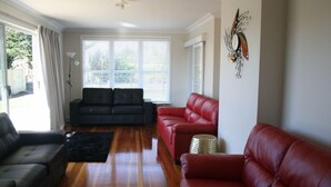 Una sala de estar con un sofá gris oscuro, un sofá rojo y un sofá negro. Hay una lámpara de pie y un adorno en la pared.