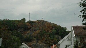 A house with a white exterior and a red roof, situated on a hillside with autumn-colored trees. - Solborg sommerpensjonat (Lindesnes)