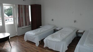 A room with two single beds, a wooden floor, a small table, and a window with curtains. - Solborg sommerpensjonat (Lindesnes)