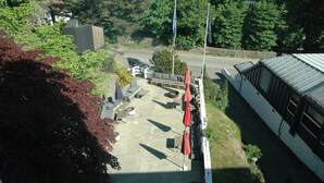 An outdoor patio area with seating and umbrellas, surrounded by trees and a road. - Solborg sommerpensjonat (Lindesnes)