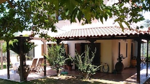 Ein überdachter Patio-Bereich mit Gartenmöbeln, einer Pergola und Blumentöpfen.