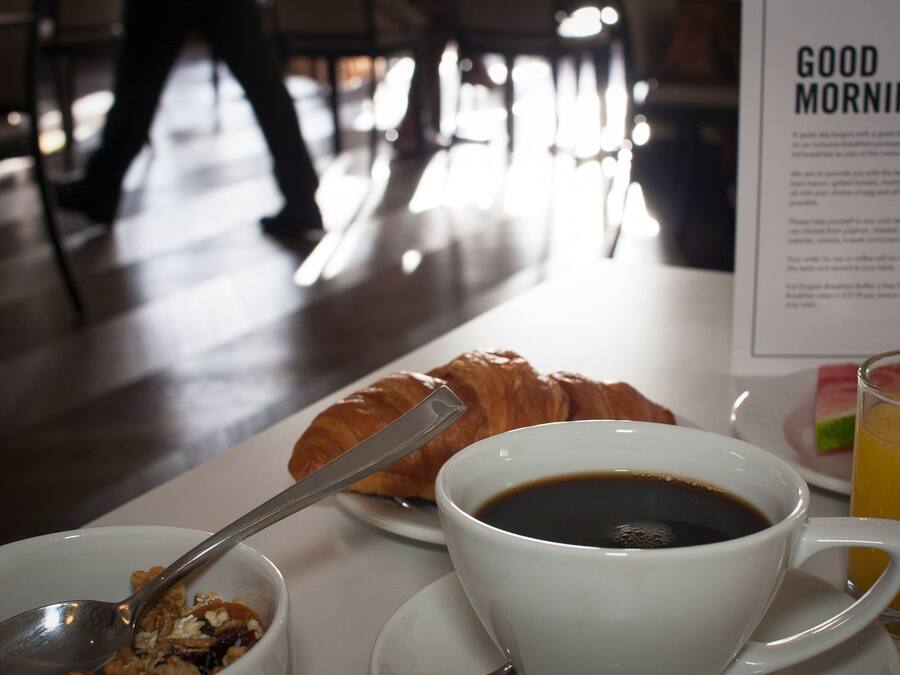 Une table dressée pour le petit-déjeuner, avec un croissant, du café et du jus de fruits.