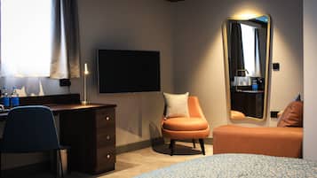 A hotel room with a bed, a desk, a chair, a dresser, a mirror, and a television.