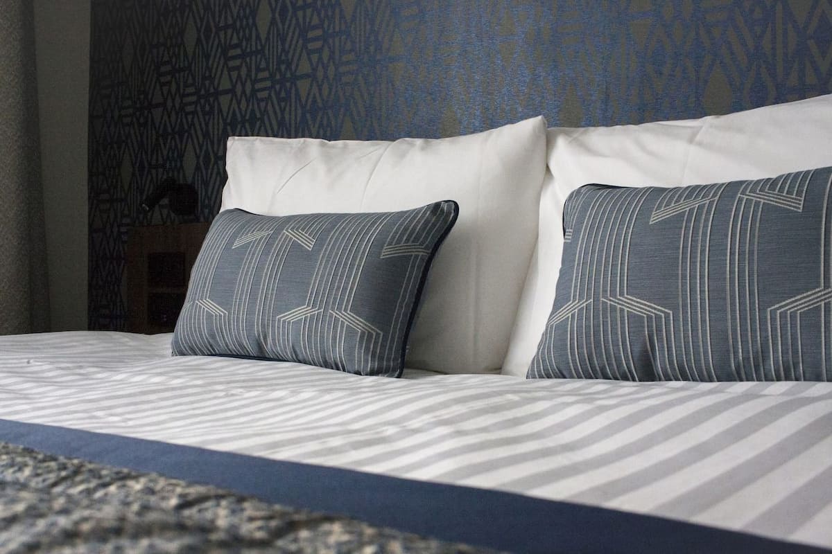 A bed with striped bedding and two pillows with geometric patterns.