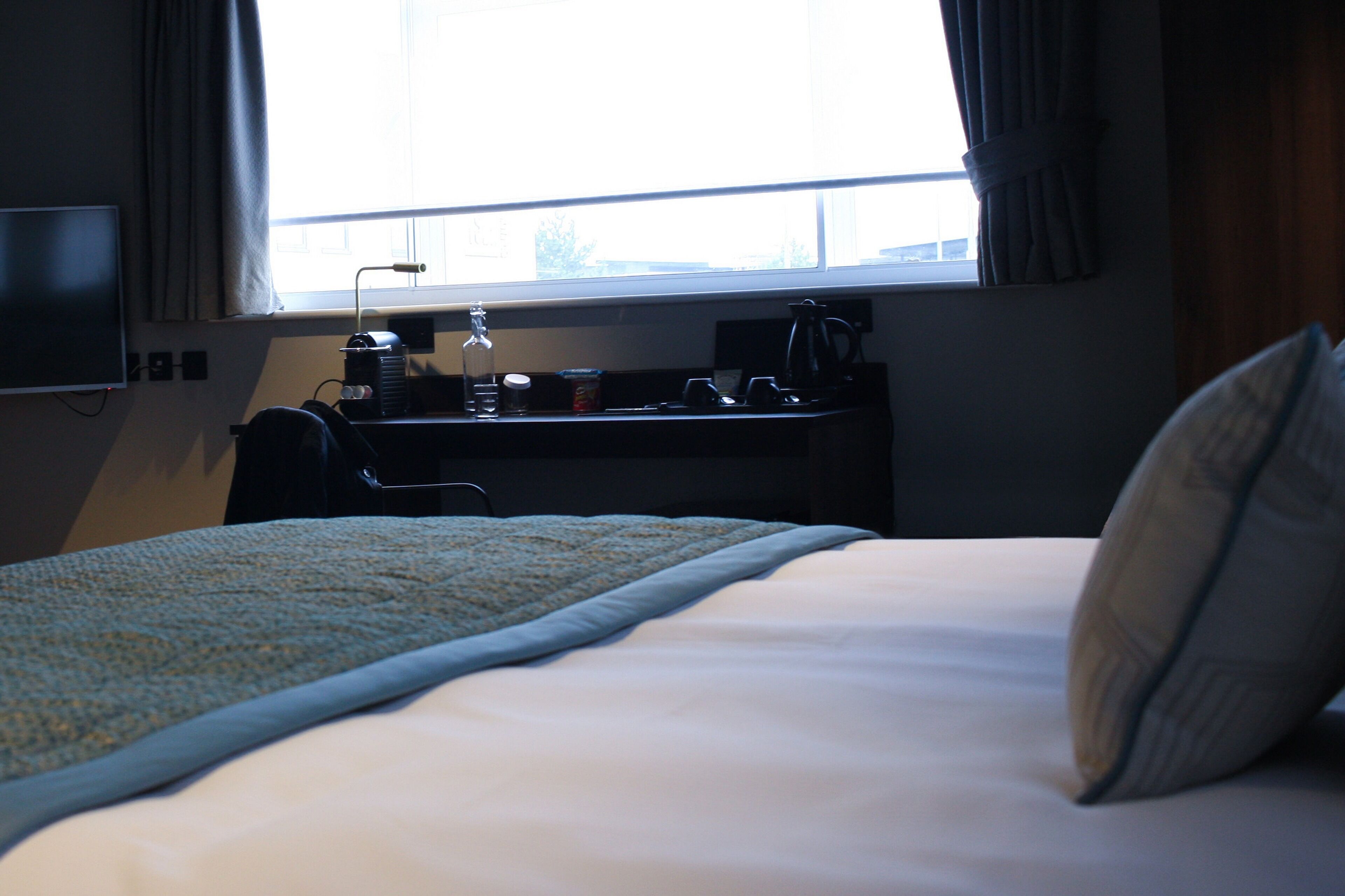 A hotel room with a bed, a desk with a computer, and a window with curtains.