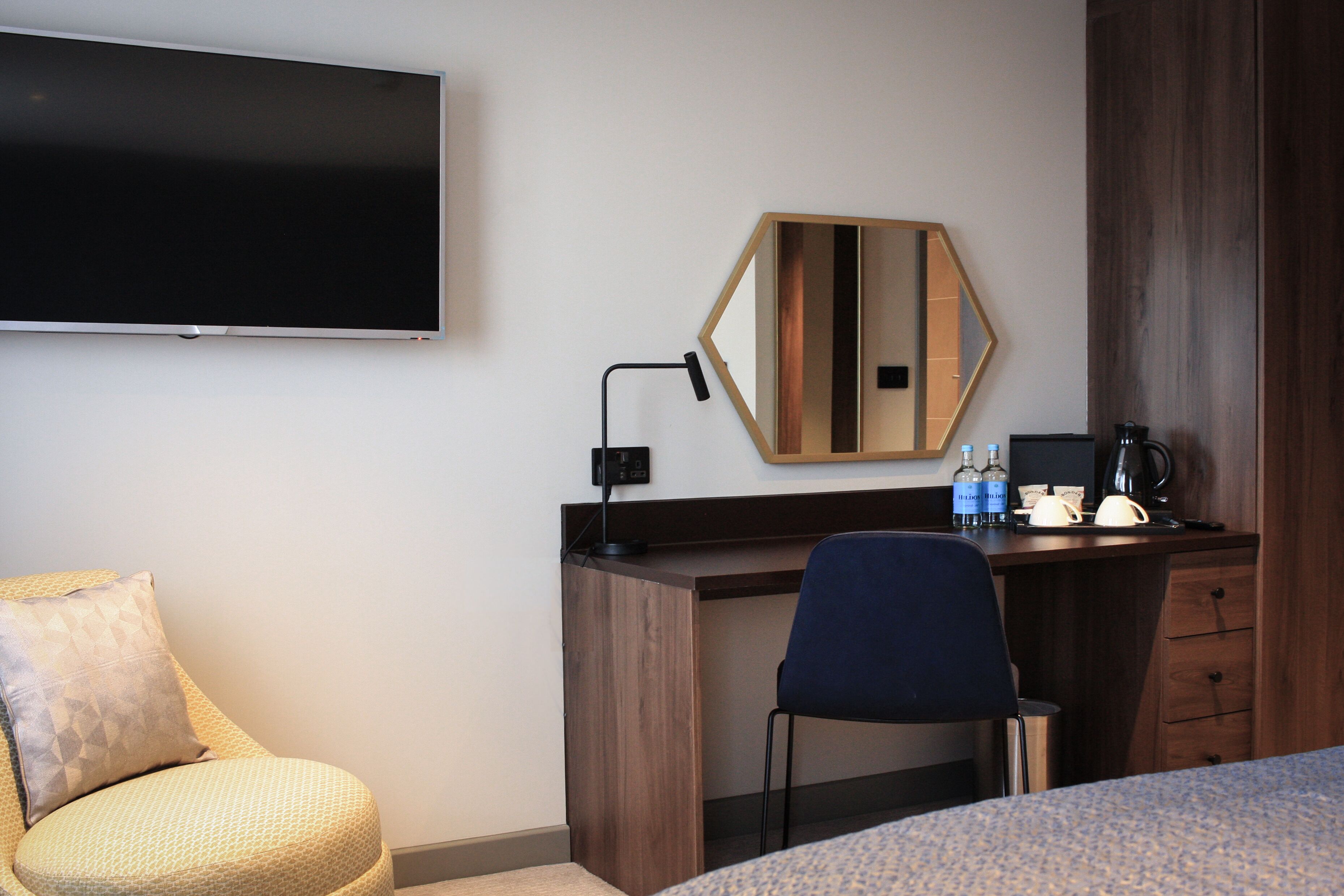 A hotel room with a bed, a desk, a chair, a television, a mirror, and a coffee maker.
