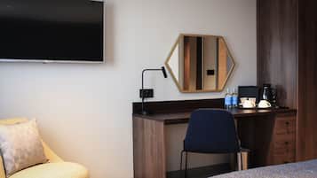 A hotel room with a bed, a desk, a chair, a television, a mirror, and a coffee maker.
