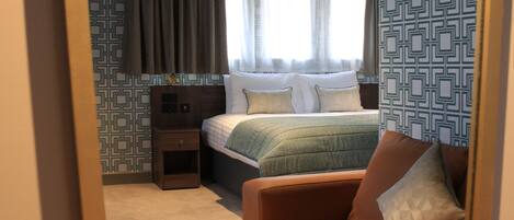 A bedroom with a bed, a nightstand, a chair, and patterned wallpaper.