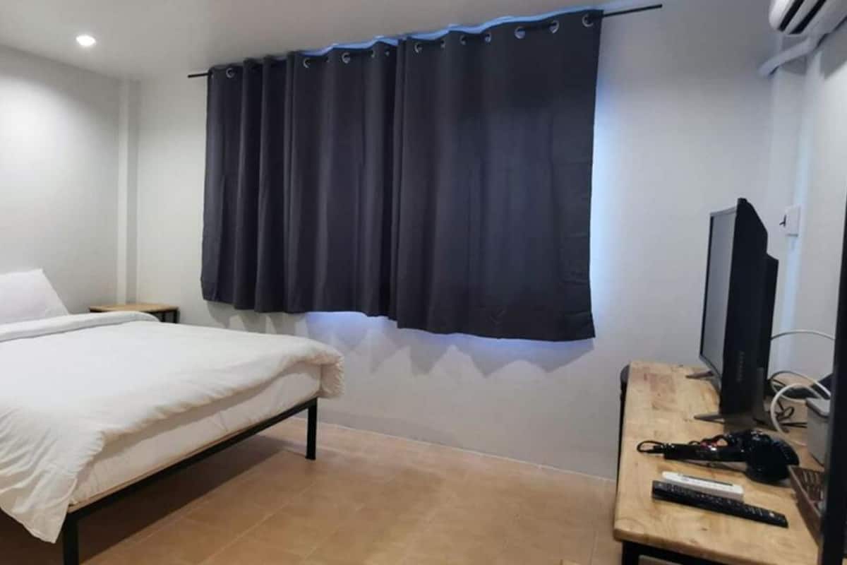 Quarto com cama, mesas de cabeceira, televisão e janela com cortinas.