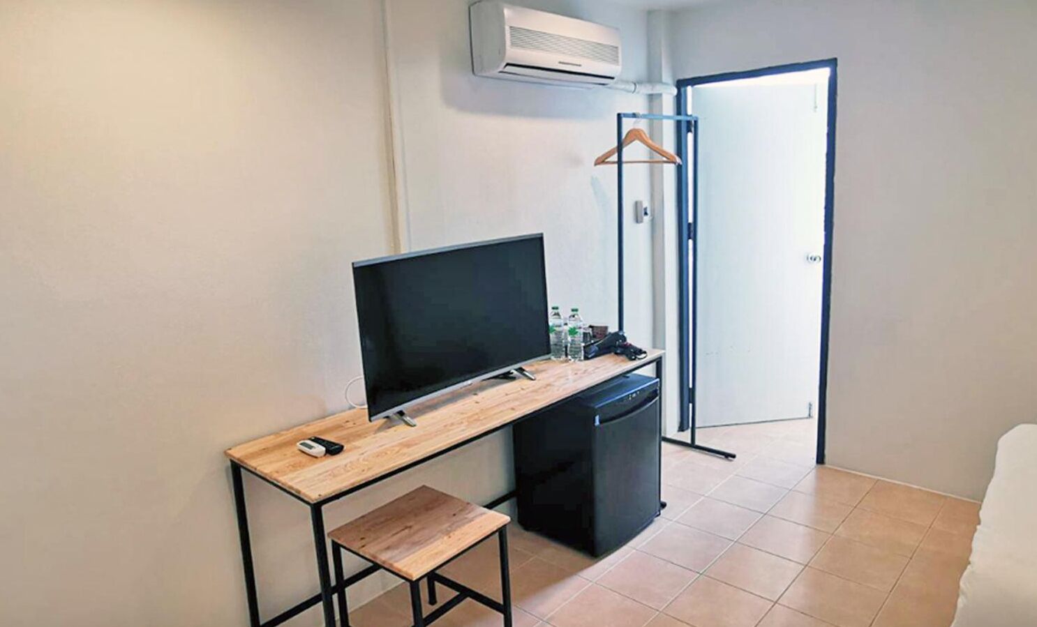 A small, modern room with a wooden desk, a flat-screen TV, a small black cabinet, and a hanging clothes rack.