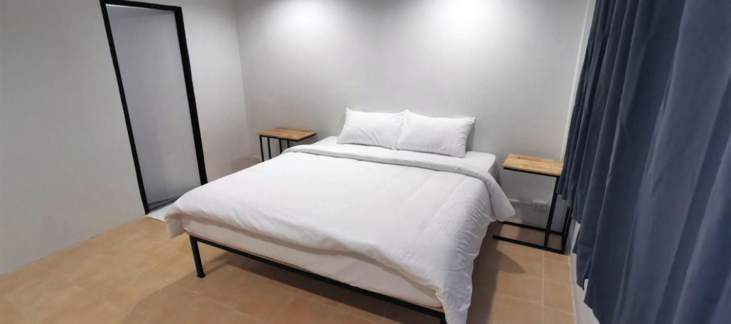 A bedroom with a bed, two bedside tables, a mirror, and a curtain.