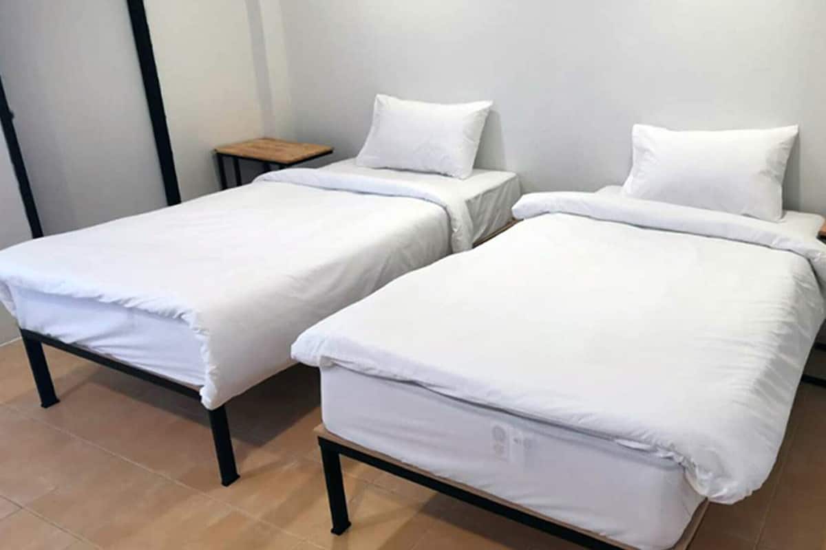 Duas camas de solteiro com roupa de cama branca, mesinhas de cabeceira de madeira e chão em azulejos.
