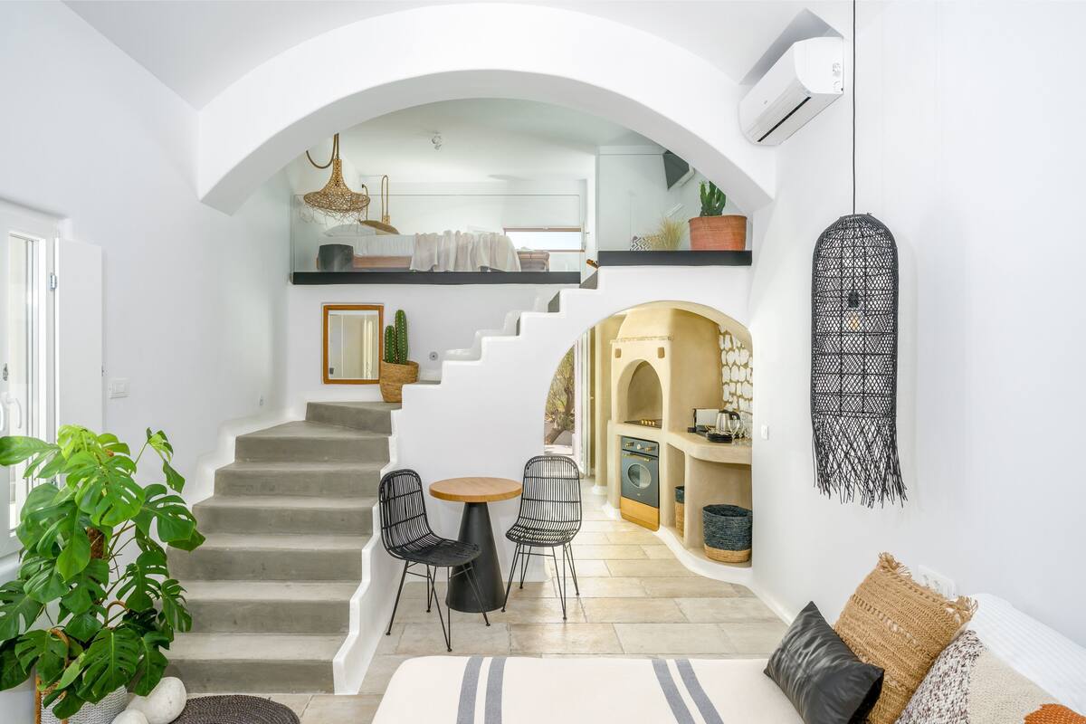 A modern interior with a staircase leading to a loft bedroom, a dining area with two chairs, and a living space with a sofa and cushions.