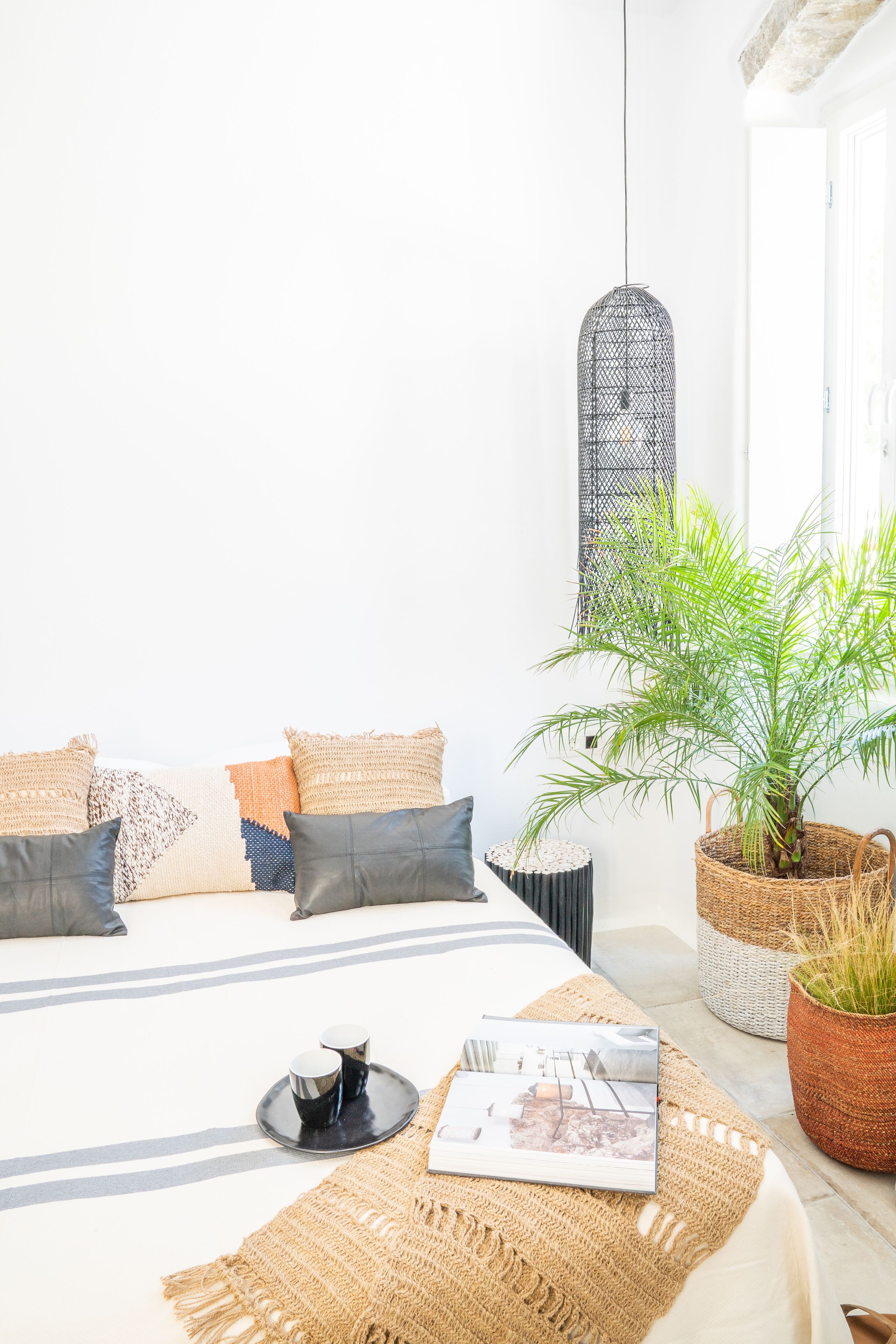 A neatly arranged bedroom with a bed, pillows, a woven rug, a potted plant, and a hanging light fixture.