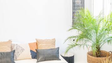 A neatly arranged bedroom with a bed, pillows, a woven rug, a potted plant, and a hanging light fixture.