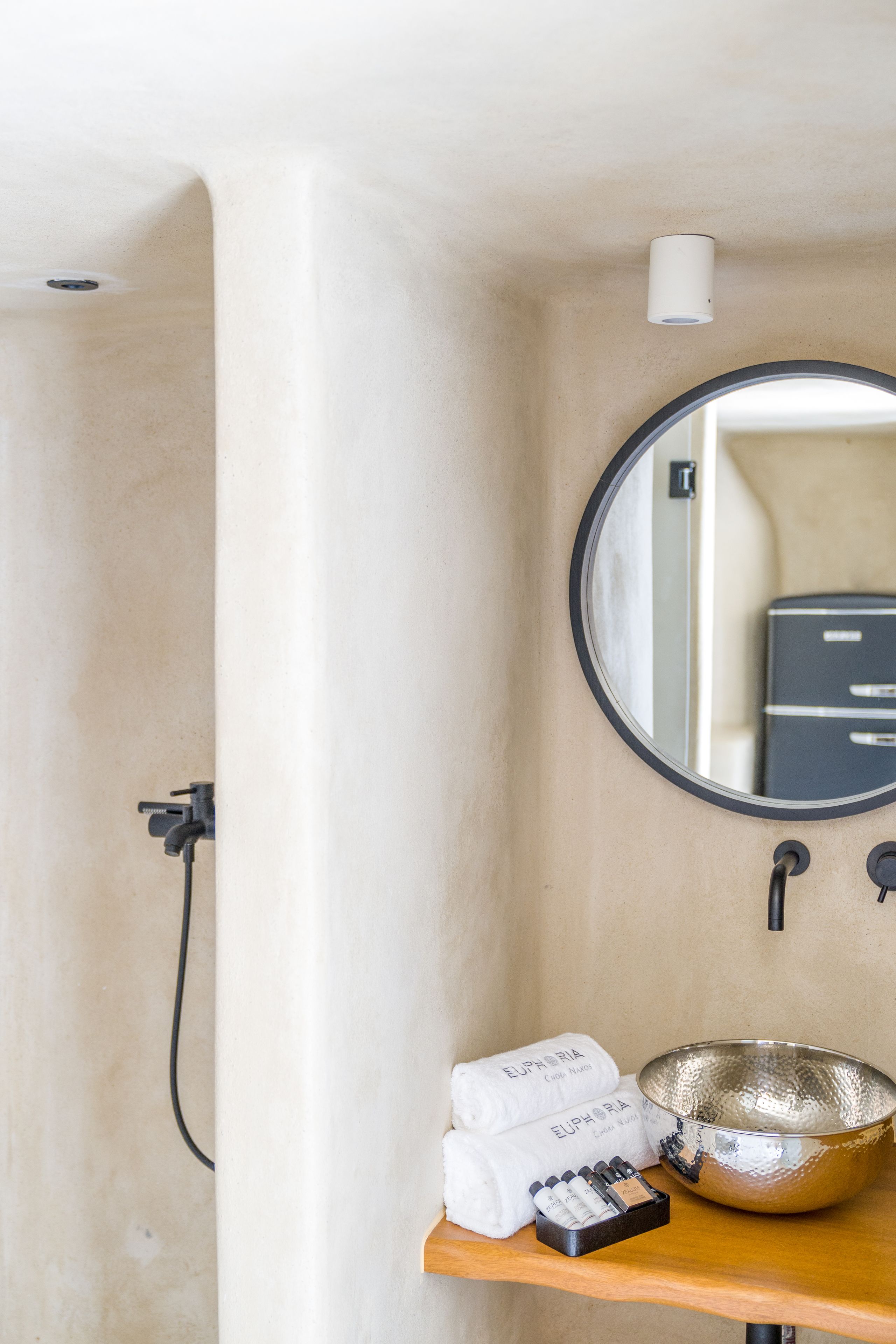 Un baño con bañera, un espejo redondo, un lavabo y artículos de aseo en un estante.