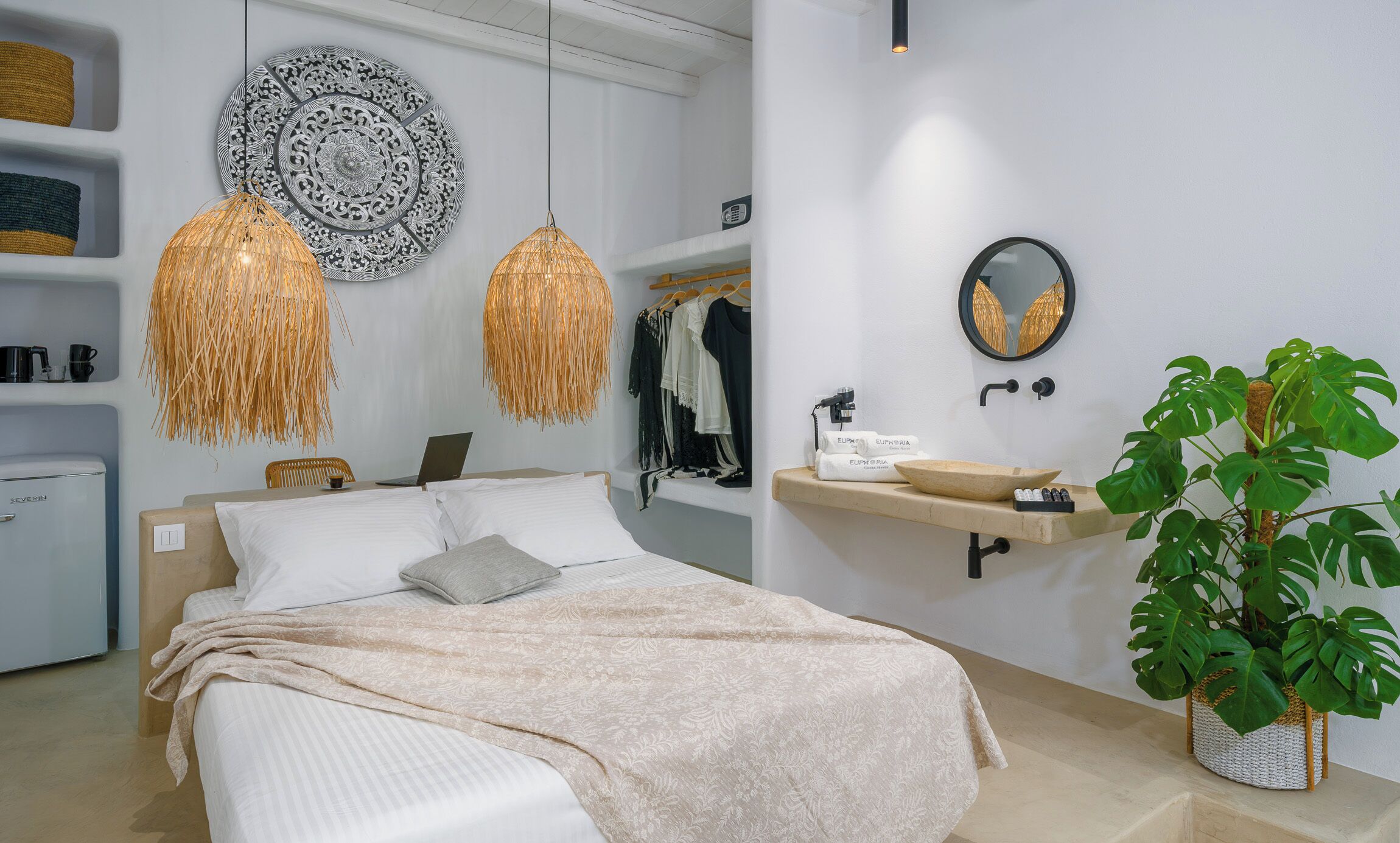 Quarto moderno com cama, mesa de cabeceira, abajur, guarda-roupa, espelho e um vaso com planta.