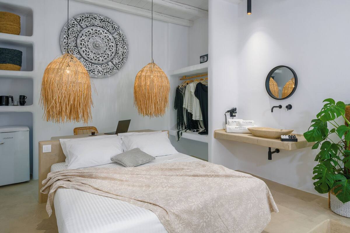 A modern bedroom with a bed, bedside table, lamp, wardrobe, mirror, and a potted plant.