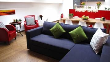 A modern living room with a dark blue sofa, red chairs, and a dining area with a red and white color scheme.