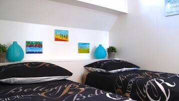Une chambre avec deux lits, chacun agrémenté de draps à motifs noir et blanc. Trois tableaux sont accrochés au mur au-dessus des lits, et deux vases bleus sont posés sur la table de chevet.