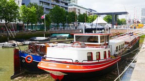 A red and white boat docked at a marina with a cityscape in the background. - Boathotel Rotterdam Seven (Rotterdam)
