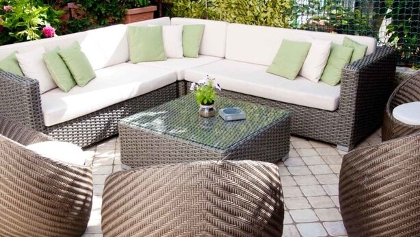 A sectional sofa with green cushions, a glass-top coffee table, and wicker chairs in an outdoor patio setting. - Hotel Marinella (Celle Ligure)