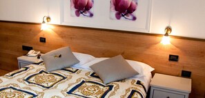 Una cama bien tendida con ropa de cama estampada y dos almohadas, flanqueada por mesitas de noche con lámparas y un teléfono.