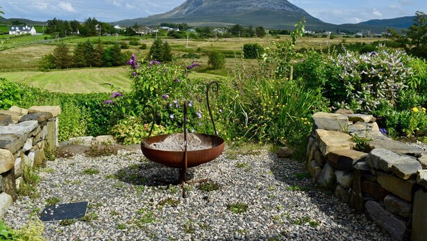 A garden with a stone wall, a metal fire pit, and a view of a mountain. - The Song House (Falcarragh)