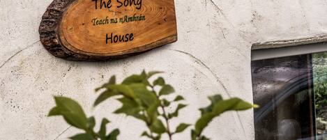 A wooden sign with the text "The Song Teach n Amhrán House" mounted on a textured wall.