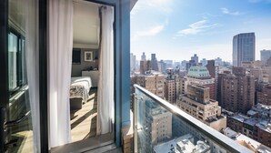 Une chambre d’hôtel située dans un immeuble de grande hauteur, offrant une vue sur la ville, dotée de grandes fenêtres et d’un balcon avec une balustrade en verre.