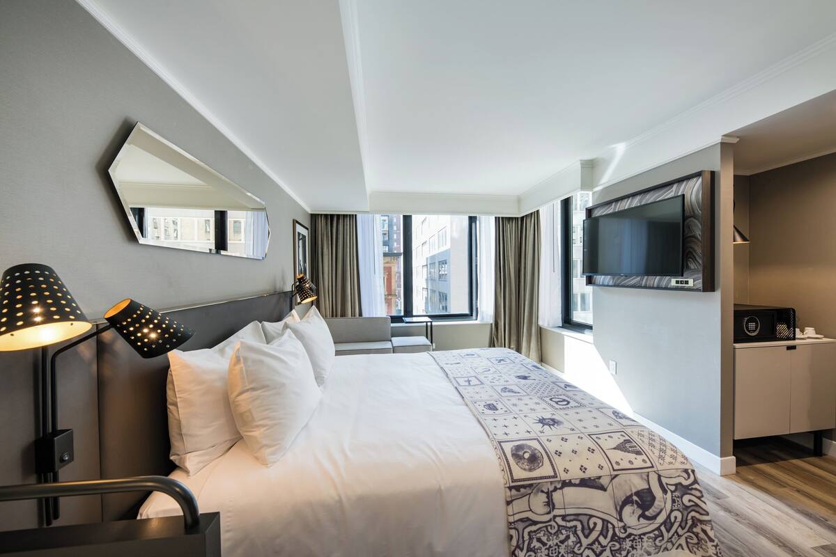 Ein Hotelzimmer mit einem Bett, einem Schreibtisch, einem Fernseher und einem Fenster mit Vorhängen.