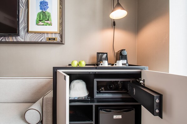 A compact hotel room with a kitchenette, a framed artwork on the wall, and a ceiling-mounted light fixture.