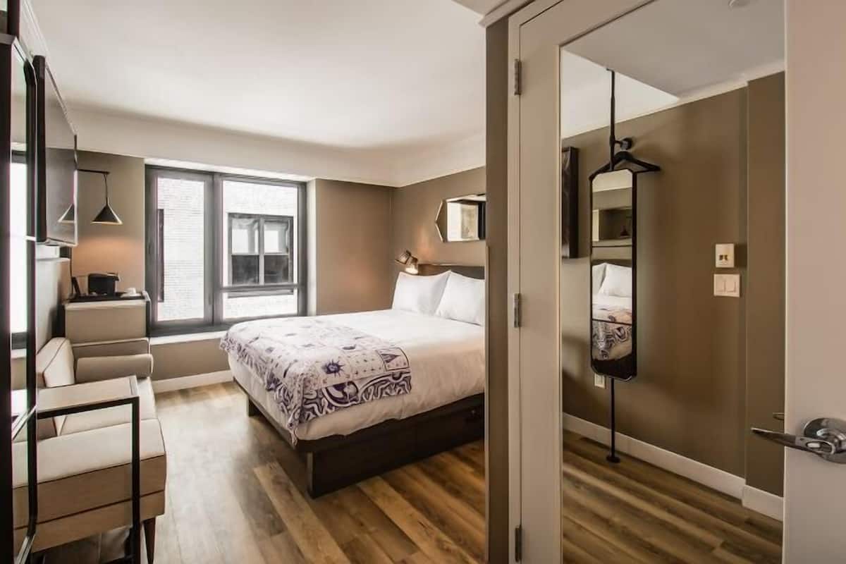 Ein Schlafzimmer mit Bett, Schreibtisch, Stuhl, Fenster und Spiegel.
