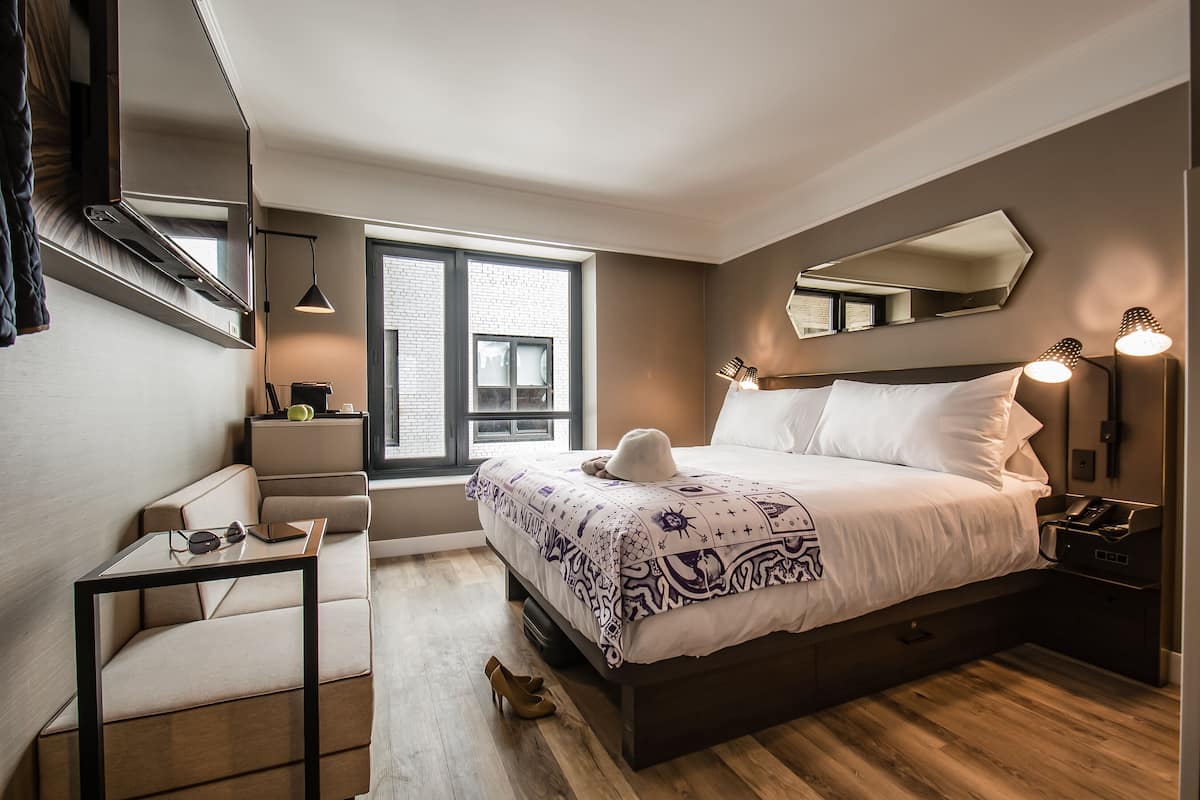 Ein modernes Schlafzimmer mit einem großen Bett, Nachttischlampen, einem Schreibtisch und einem Fenster mit Blick auf die Stadt.