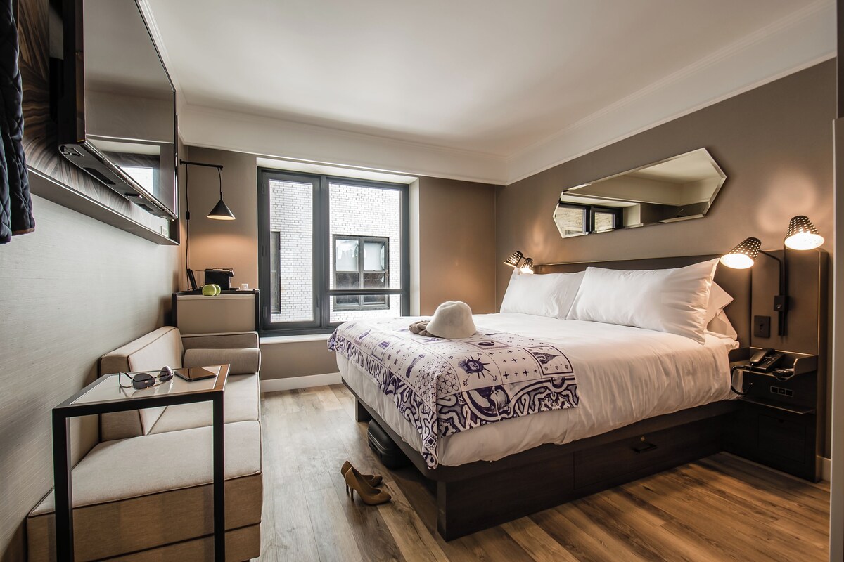 Ein modernes Schlafzimmer mit einem großen Bett, Nachttischlampen, einem Schreibtisch und einem Fenster mit Blick auf die Stadt.