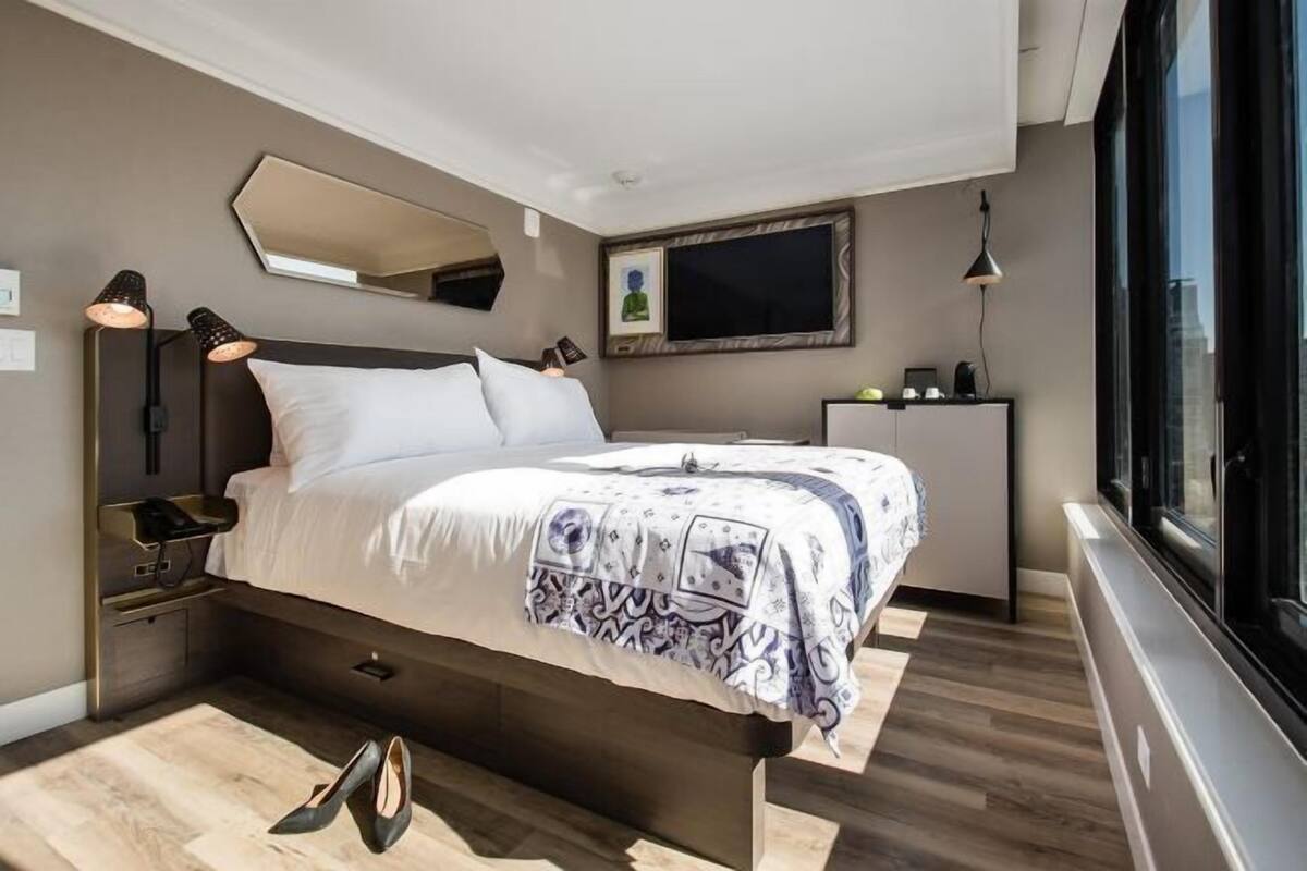 Ein modernes Schlafzimmer mit einem Bett, Nachttischlampen, einem Spiegel, einem Fernseher und einem Fenster.