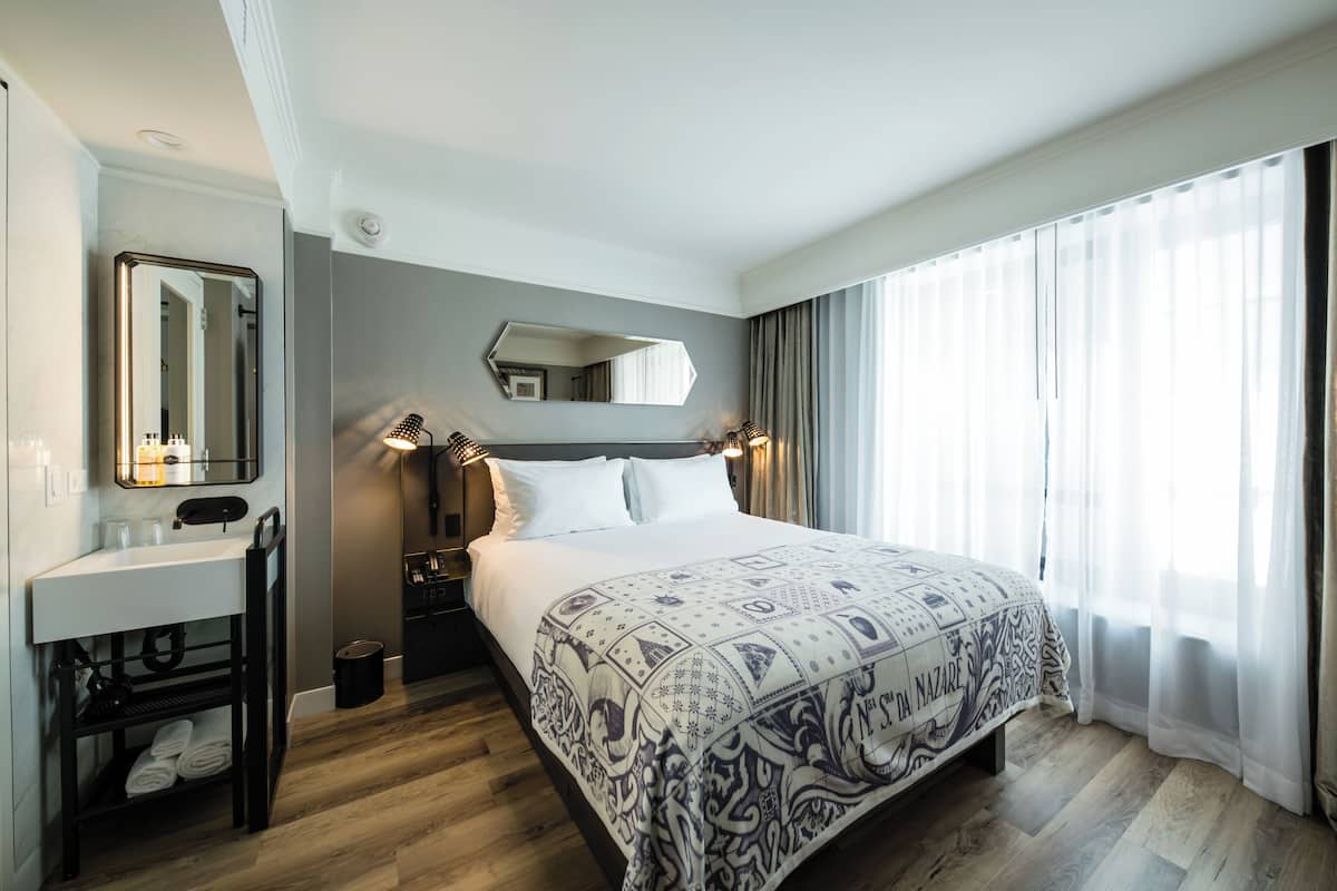 Ein Hotelzimmer mit einem großen Bett, einem Nachttisch, einem Spiegel, einer kleinen Badeinrichtung und einem Fenster mit Vorhängen.