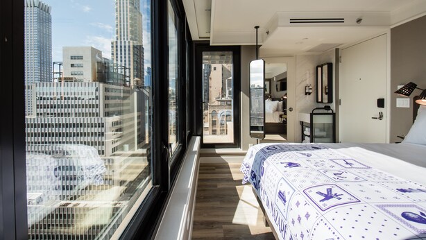 Une chambre d’hôtel moderne dotée d’une grande fenêtre donnant sur la ville, d’un lit parfaitement fait et d’un dressing.