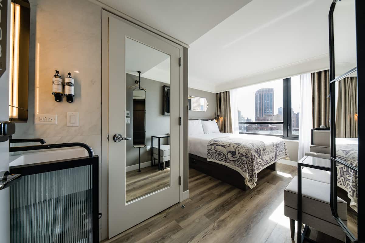 Ein Hotelzimmer mit Bett, Schreibtisch, Stuhl, Spiegel und Blick auf die Stadt.
