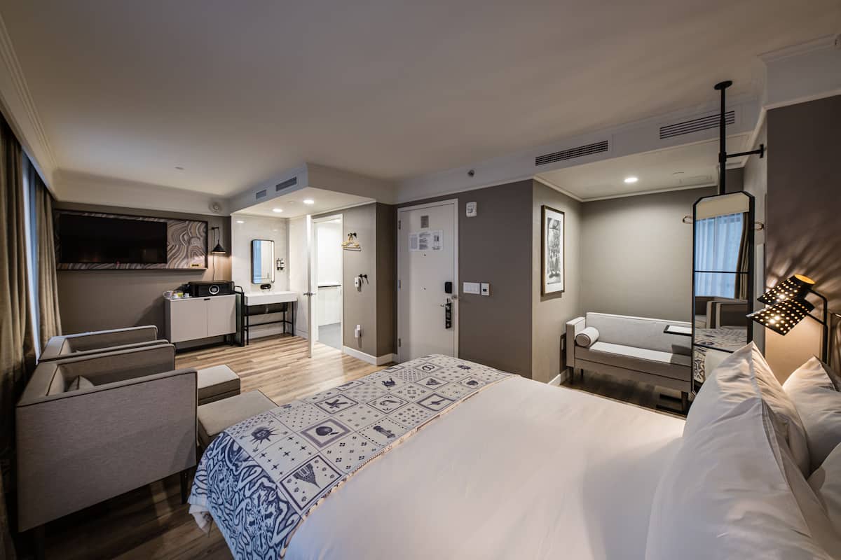 Ein modernes Hotelzimmer mit einem großen Bett, einem Schreibtisch, einem Sessel und einem Fernseher.