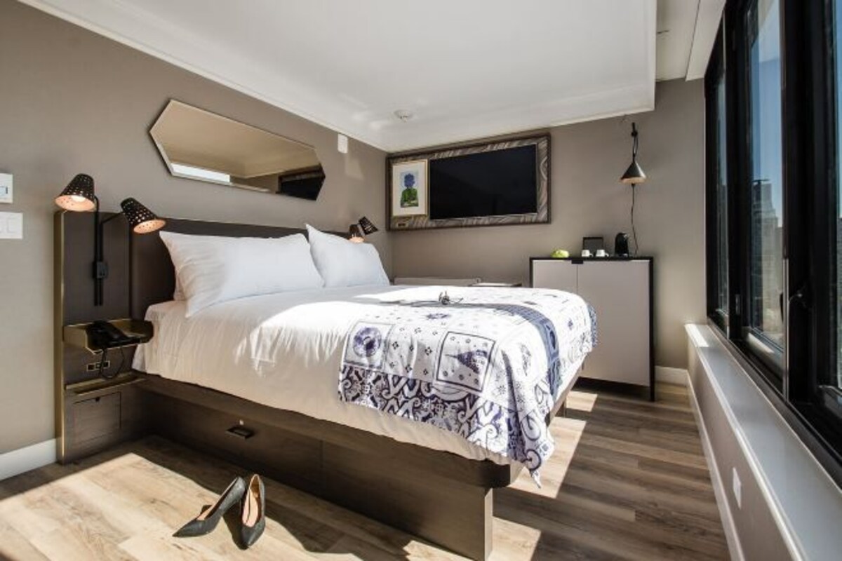 Une chambre à coucher moderne, avec un lit, des lampes de chevet, un miroir, une télévision et une fenêtre.