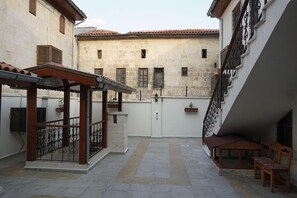 Un patio con zona de estar cubierta, una verja blanca y suelo de piedra.