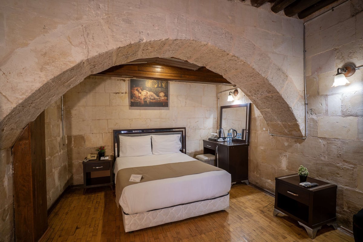 Un dormitorio con cama, mesita de noche, cómoda, espejo y un cuadro en la pared.