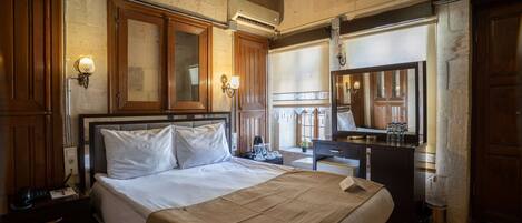 Una habitación de hotel con una cama grande, un armario de madera, una mesita de noche y un espejo.
