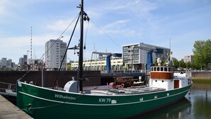 Un barco verde llamado 'Wilhelmina' atracado en un muelle, con un paisaje urbano al fondo.