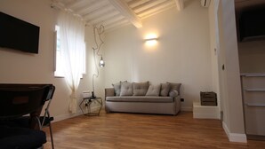 A living room with a sofa, a chair, a lamp, and a flat-screen TV mounted on the wall. - Tornabuoni Loft Apartment (Firenze)