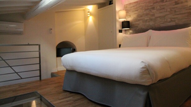 A bedroom with a bed, a wooden headboard, a wall-mounted lamp, and a small table. - Tornabuoni Loft Apartment (Firenze)